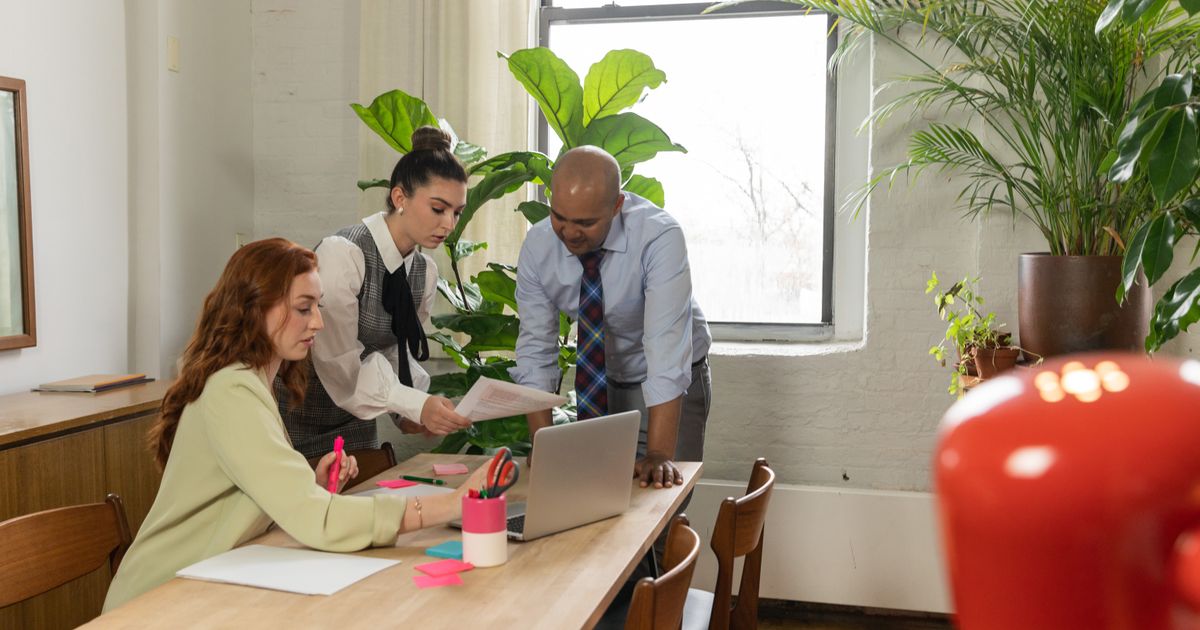 Three people talking at a laptop in an office full of plants