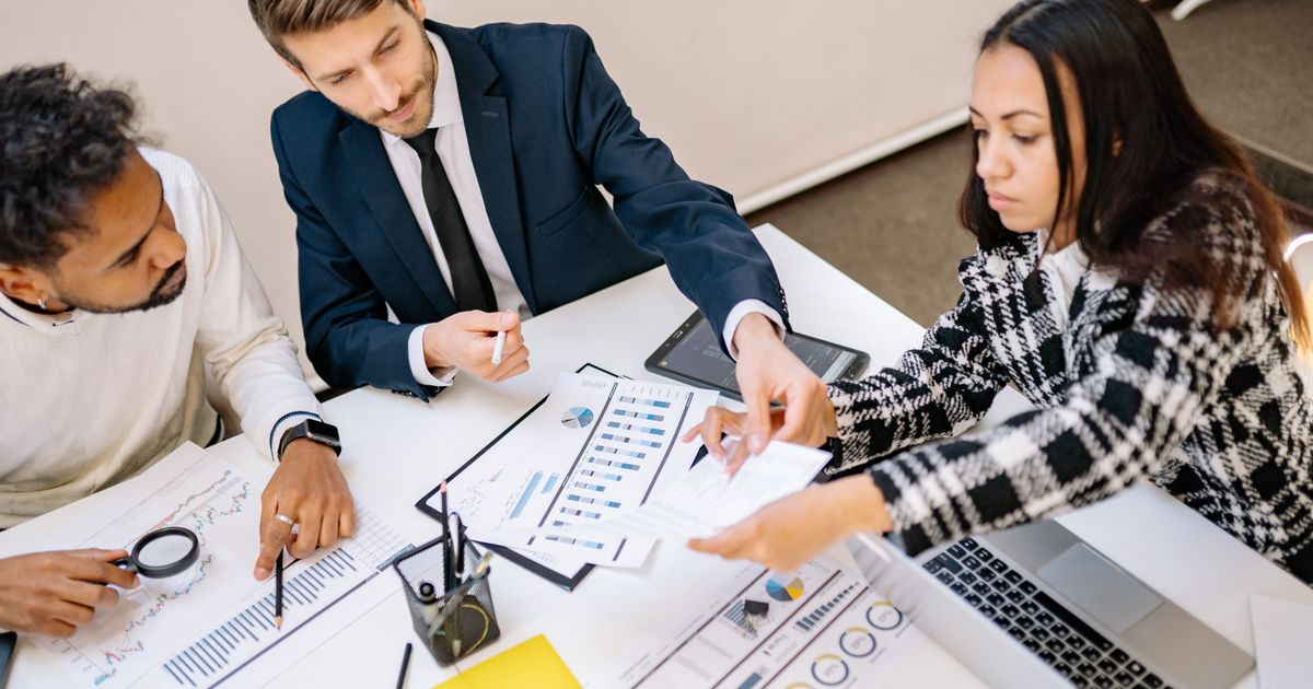 Three colleagues reviewing printed charts and figures around a table with a laptop