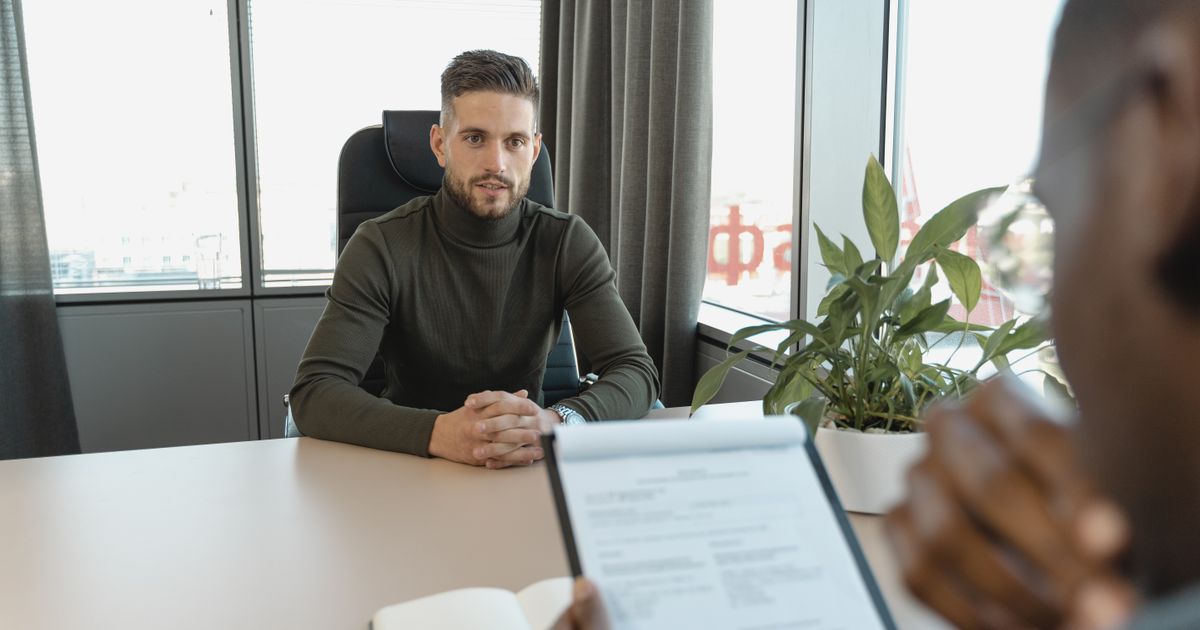 A candidate talking with an interviewer holding a resume at a desk