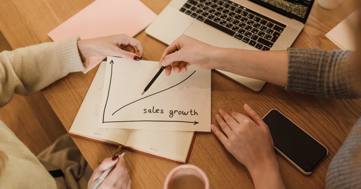 Two people at a desk with a hand-drawn sales growth chart, a laptop and a phone